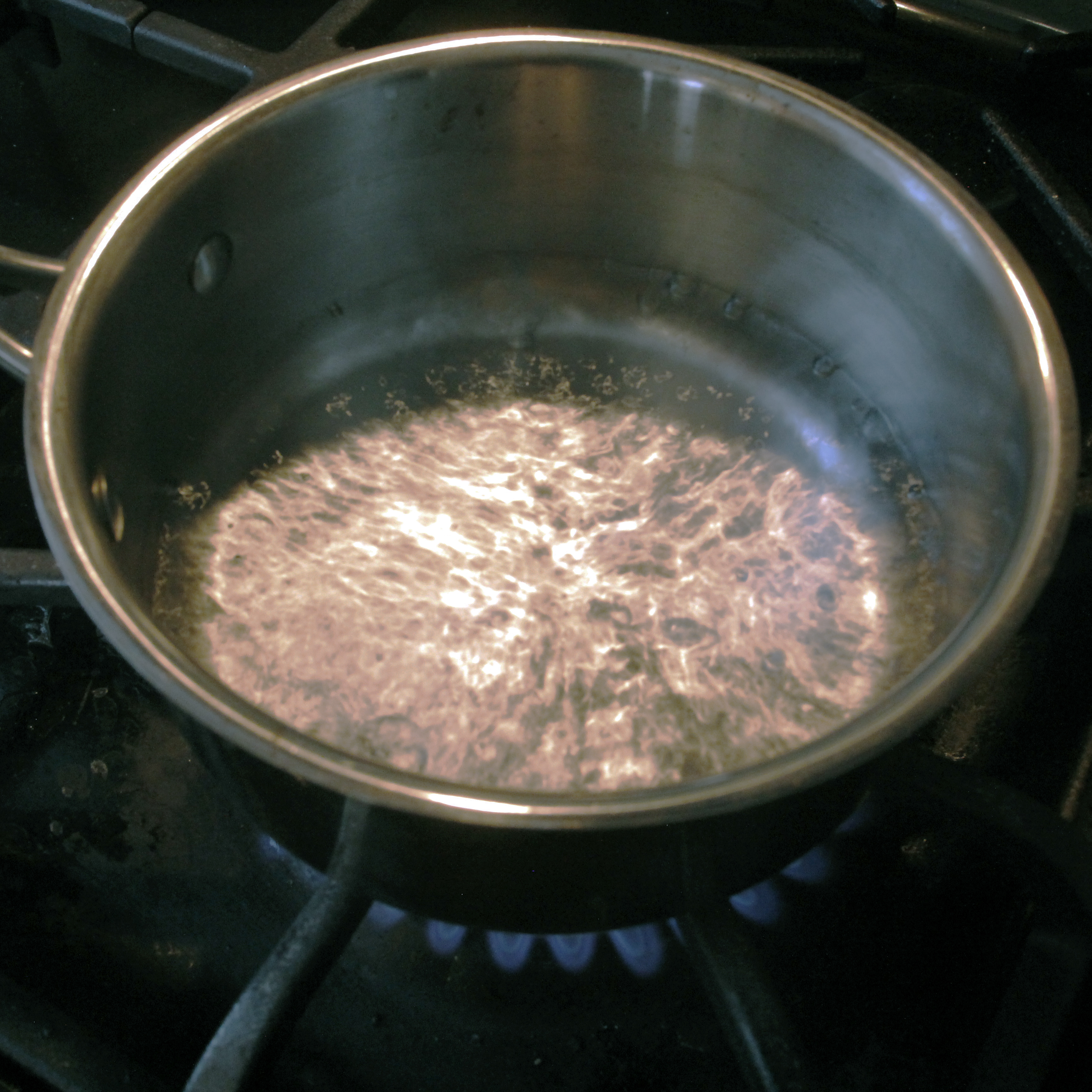 Water boiling in a metal pot over a blue flame